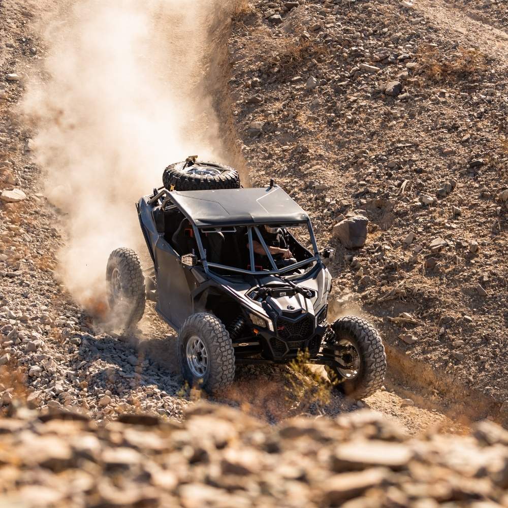 UTV driving downhill on rocky and desert terrain with dust coming up in the background. EFX MotoVator R/T tires installed.
