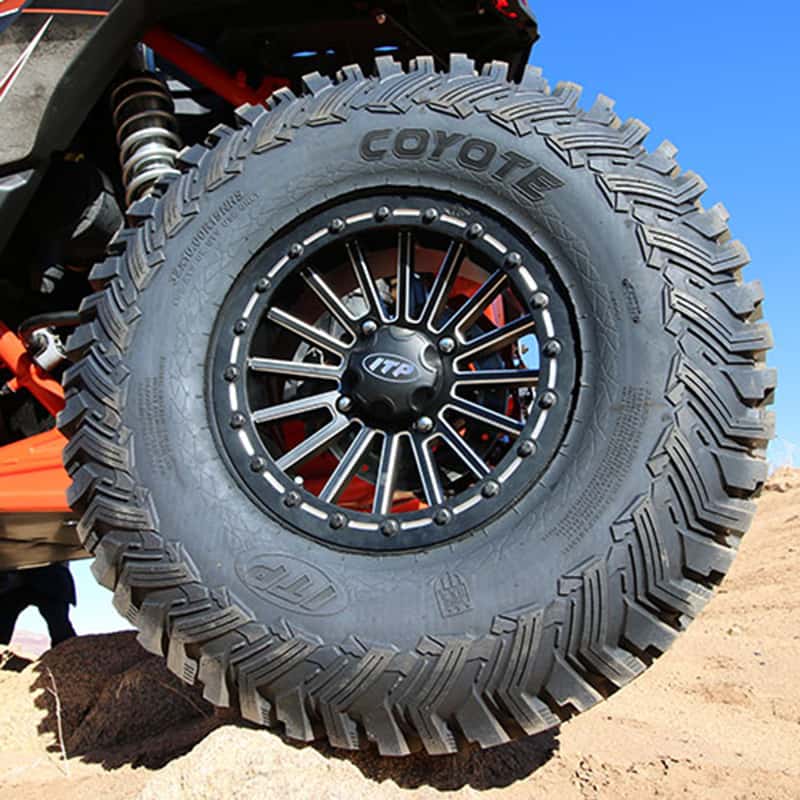 ITP Coyote radial tire installed on SXS, parked on rocks in desert.
