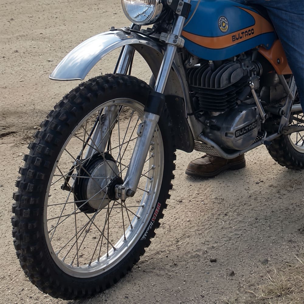 Kenda K257D Klassic motorcycle / dirt bike tire mounted on old restored Bultaco bike, parked on a gravel road.