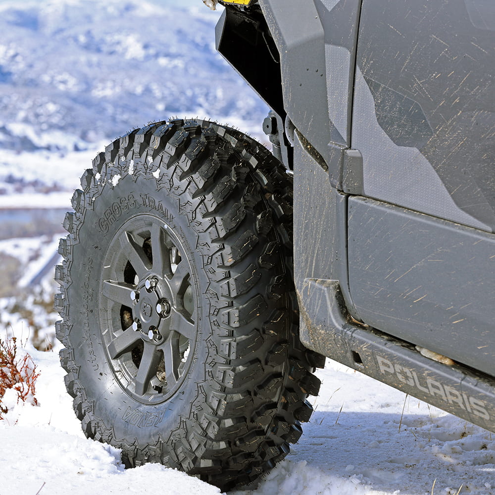 Kenda K3213 Cross Trail tire in 32x10R15 size mounted on Polaris Xpedition UTV, parked in snow on mountain.