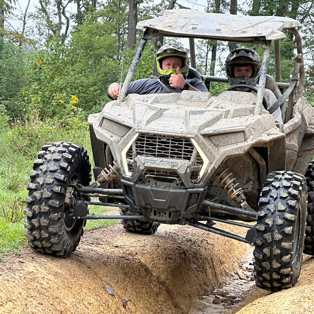 Kenda Warhawk UTV tires mounted and installed on a Polaris RZR, navigating a deep, rutted trail, undergoing a thorough testing and review process to ensure ruggedness and reliability for all customers.