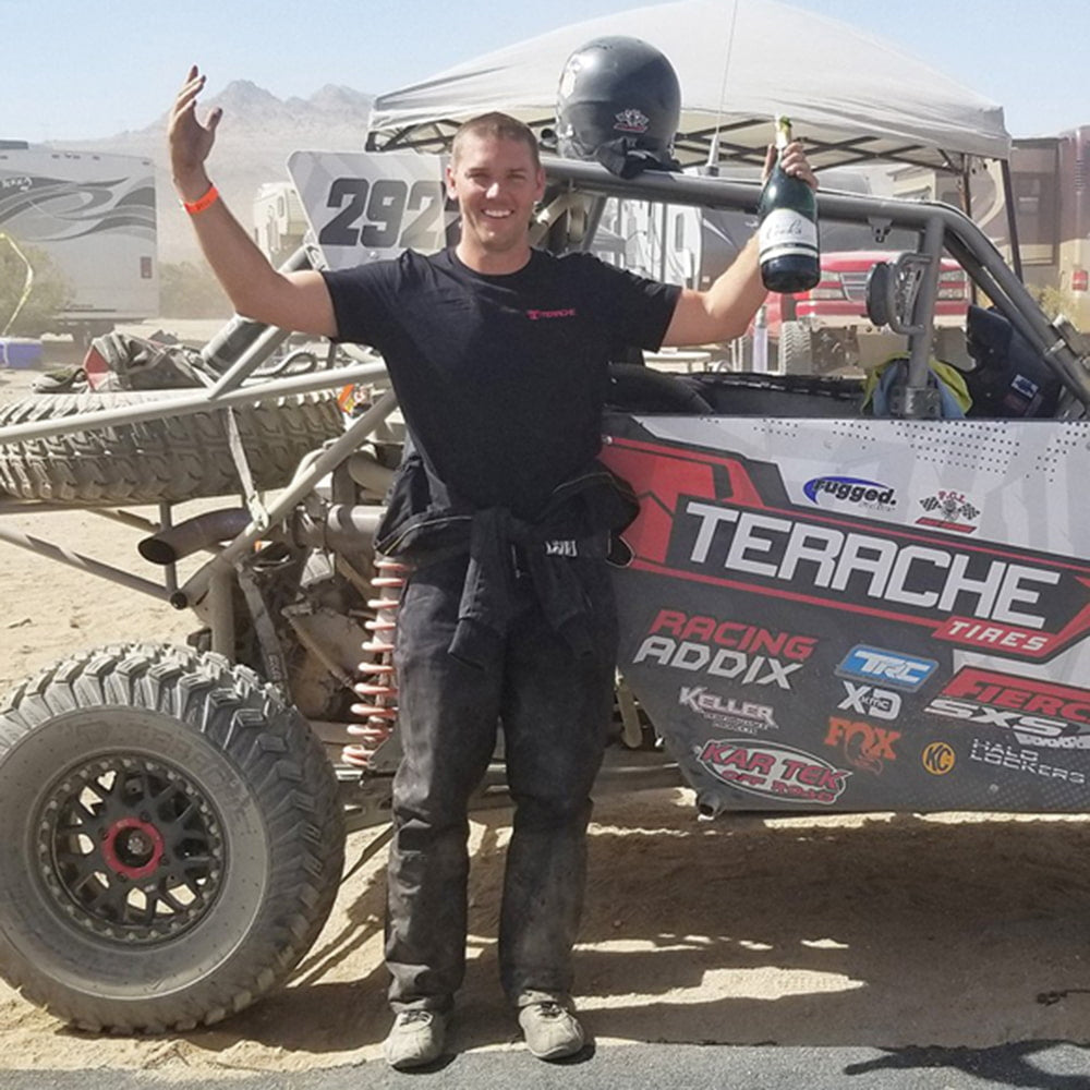 Side-by-side racer celebrating beside his Polaris RZR in the desert, featuring the Terache Stryker race tires.