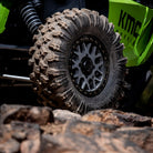 Close-up of the EFX MotoRavage off-road UTV tire with deep treads mounted on a silver multi-spoke wheel, attached to a bright green KMC Wheels vehicle on rocky terrain.