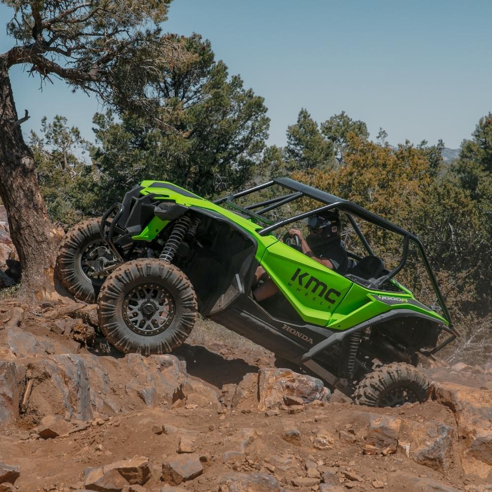 A bright green Honda X-Road 1000 off-road utility vehicle equipped with EFX MotoRavage Tires, shown as it navigates a rocky dirt trail with trees in the background.