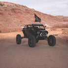 A black off-road UTV with EFX MotoRavage XL tires is parked on a dirt road in a desert landscape with rocky hills in the background. A black flag is attached to the roof.