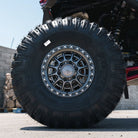 A close-up shot of a black off-road tire mounted on a Fuel UTV Cycle utv wheel in gloss gunmetal attached to a UTV undercarriage, photographed outdoors on a paved surface.