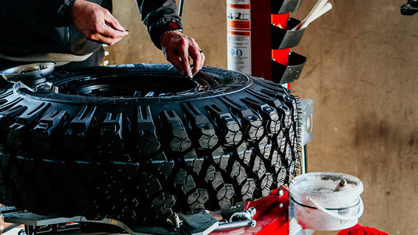 Person working on a large black Valor UTV tire with tools in a workshop setting.