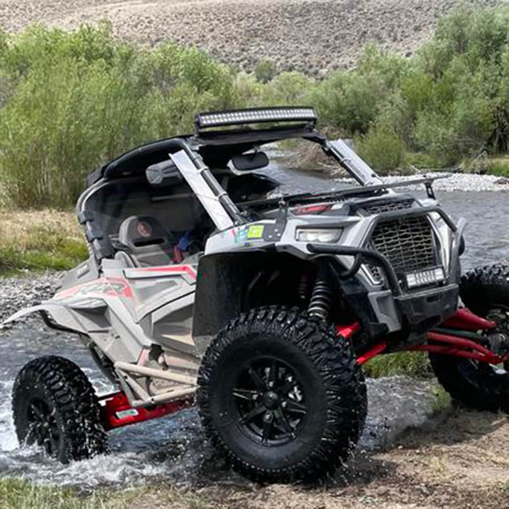 M2 Evil Radial tires mounted on Polaris RZR crossing a river stream in the wilderness.