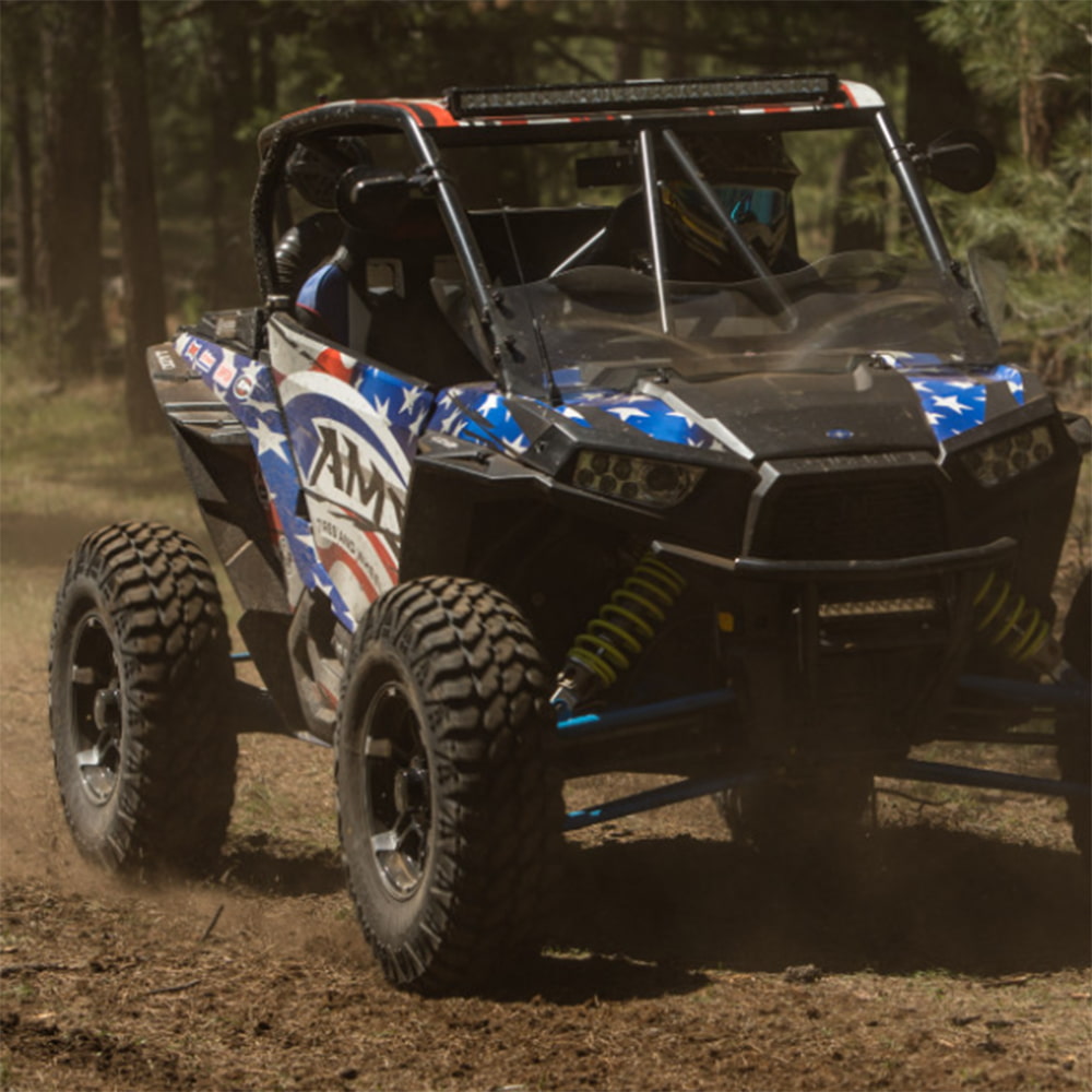 Polaris RZR driving off road on a dirt trail, with AMS M4 Evil tires installed.