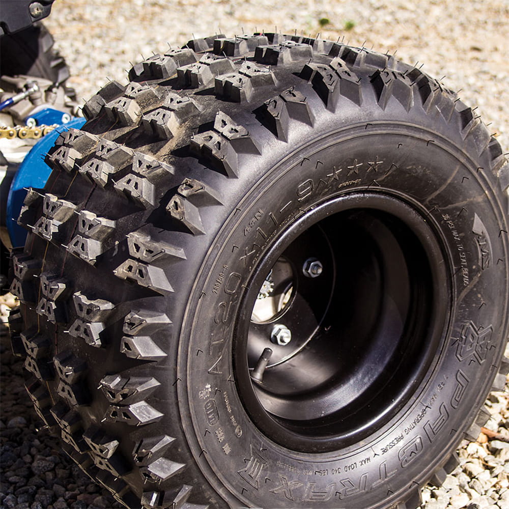 AMS Pactrax II rear tire installed and mounted on a rim, in 20x11-9 size, parked on gravel.