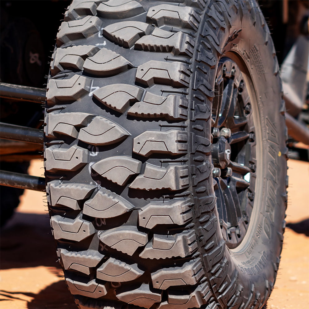Close up detailed view of the tread pattern on the Atturo Trail Blade Boss SXS tire mounted on a RZR, showcasing the serrated knife edge tread blocks and rugged shoulder to sidewall tread block design as well as the deep rim guard construction.