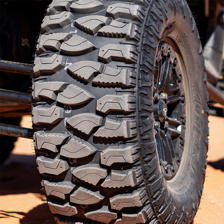 Close up detailed view of the tread pattern on the Atturo Trail Blade Boss SXS tire mounted on a RZR, showcasing the serrated knife edge tread blocks and rugged shoulder to sidewall tread block design as well as the deep rim guard construction.