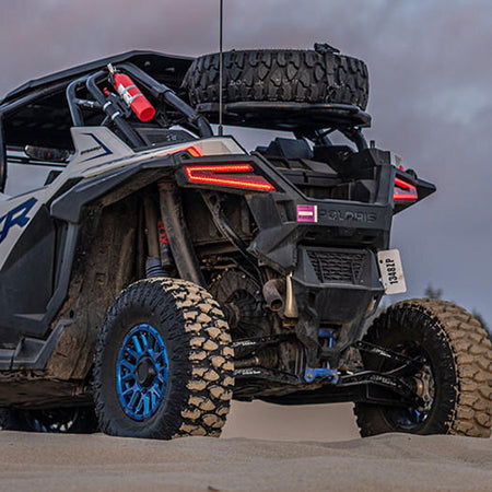 15" Atturo Trail Blade BOSS tires mounted on Polaris RZR parked at the dunes, with spare tire mounted on rack.