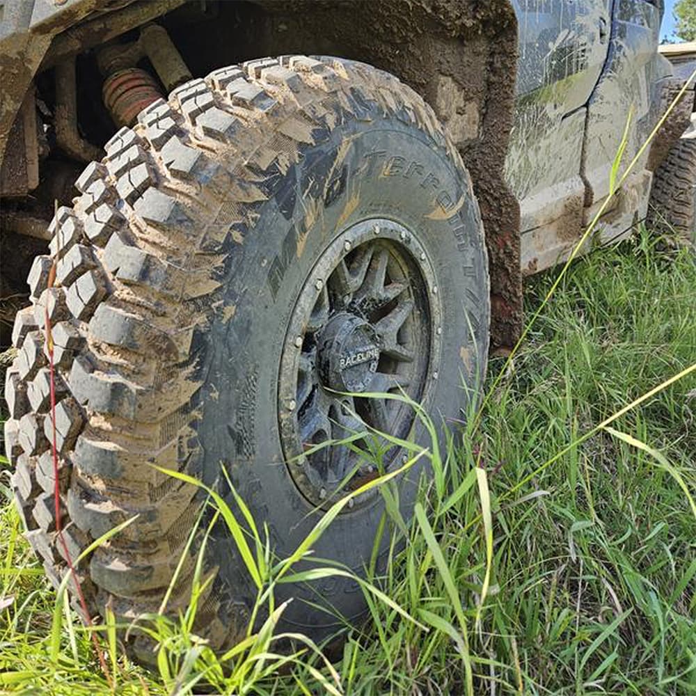 Muddy BFG KM3 all-terrain mud tire mounted on UTV parked in tall grass.