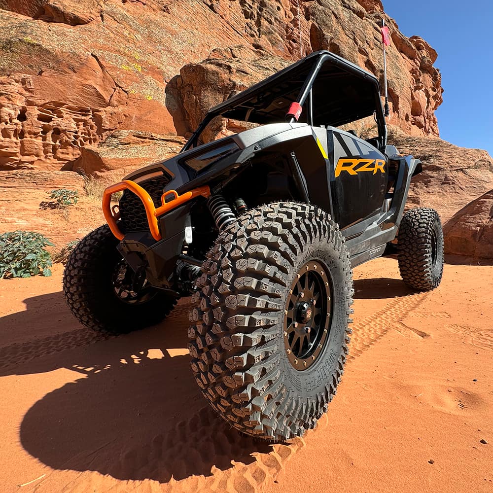 Roctane ST tires mounted on Polaris RZR parked in red sand high in the desert with rocky wall in the background.