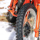 Kenda K257D Klassic front tire mounted on vintage bright orange motorcycle, parked in the snow.