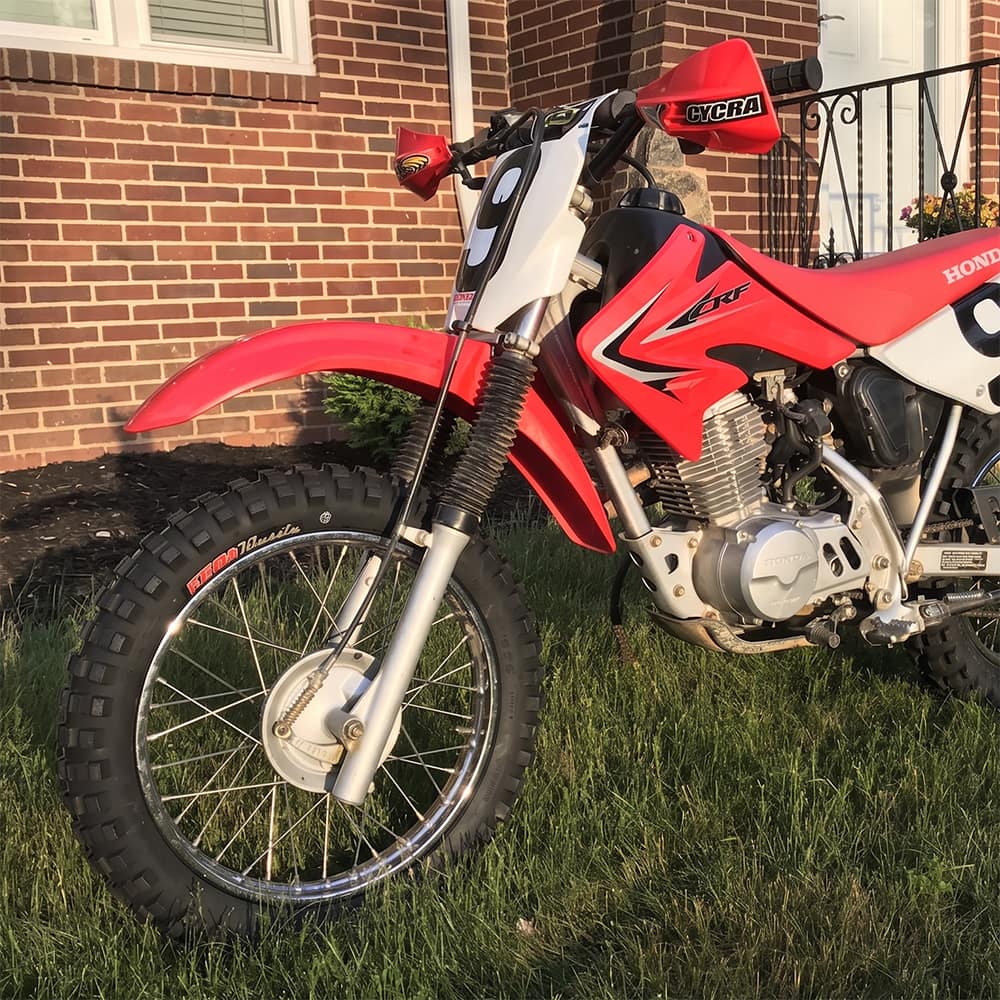 Kenda K257D Klassic tires mounted on Honda CRF80 dirt bike, parked in the the front yard of a brick house.