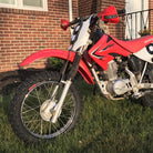 Kenda K257D Klassic tires mounted on Honda CRF80 dirt bike, parked in the the front yard of a brick house.