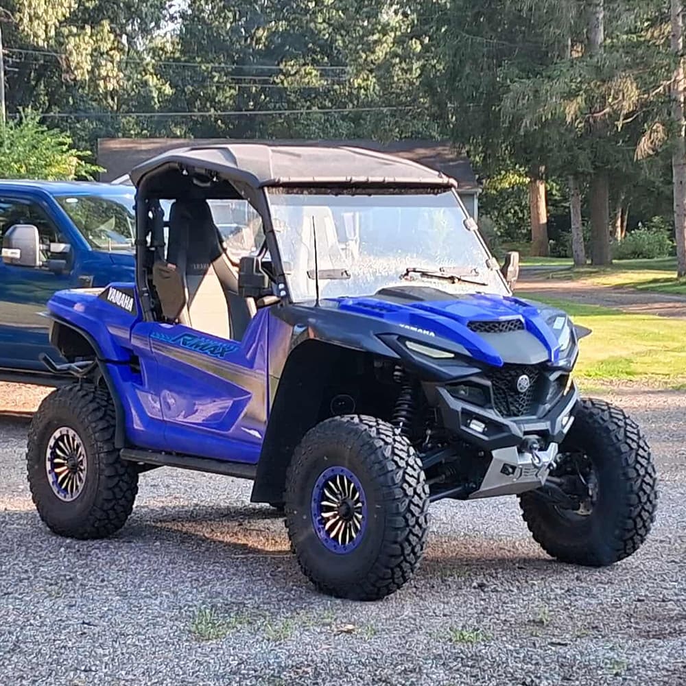 Kenda Klever XT 32x10R14 UTV steel belted radial tires sold by Ride or Die Tire, mounted on a blue Yamaha RMAX, parked in driveway.