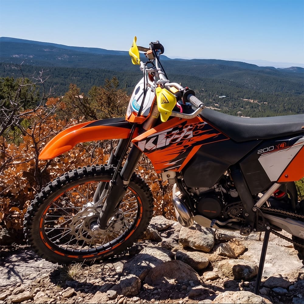 KTM 200 dirt bike parked on top of a mountain, overlooking the hills, showcasing the Kenda Millville 2 front MX / offroad tire, with durable and rugged construction and high traction design.