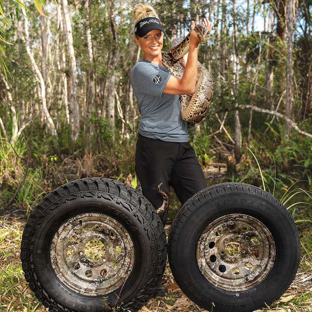 Amy Siewe posing with a python snake and Kenda TrueTimber camo trailer wheels in the Everglades.