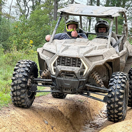 Kenda Warhawk UTV tires mounted and installed on a Polaris RZR, navigating a deep, rutted trail, undergoing a thorough testing and review process to ensure ruggedness and reliability for all customers.