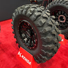 Brand new UTV tire, the Kenda Warhawk 8-ply nylon radial heavy duty aggressive off road and all terrain tire, featuring two new sizes, 32x10R14 and 33x10R15, shown here mounted on a Raceline wheel, displayed at a trade show in the Kenda booth, on a red carpet, sold by Ride or Die Tire.