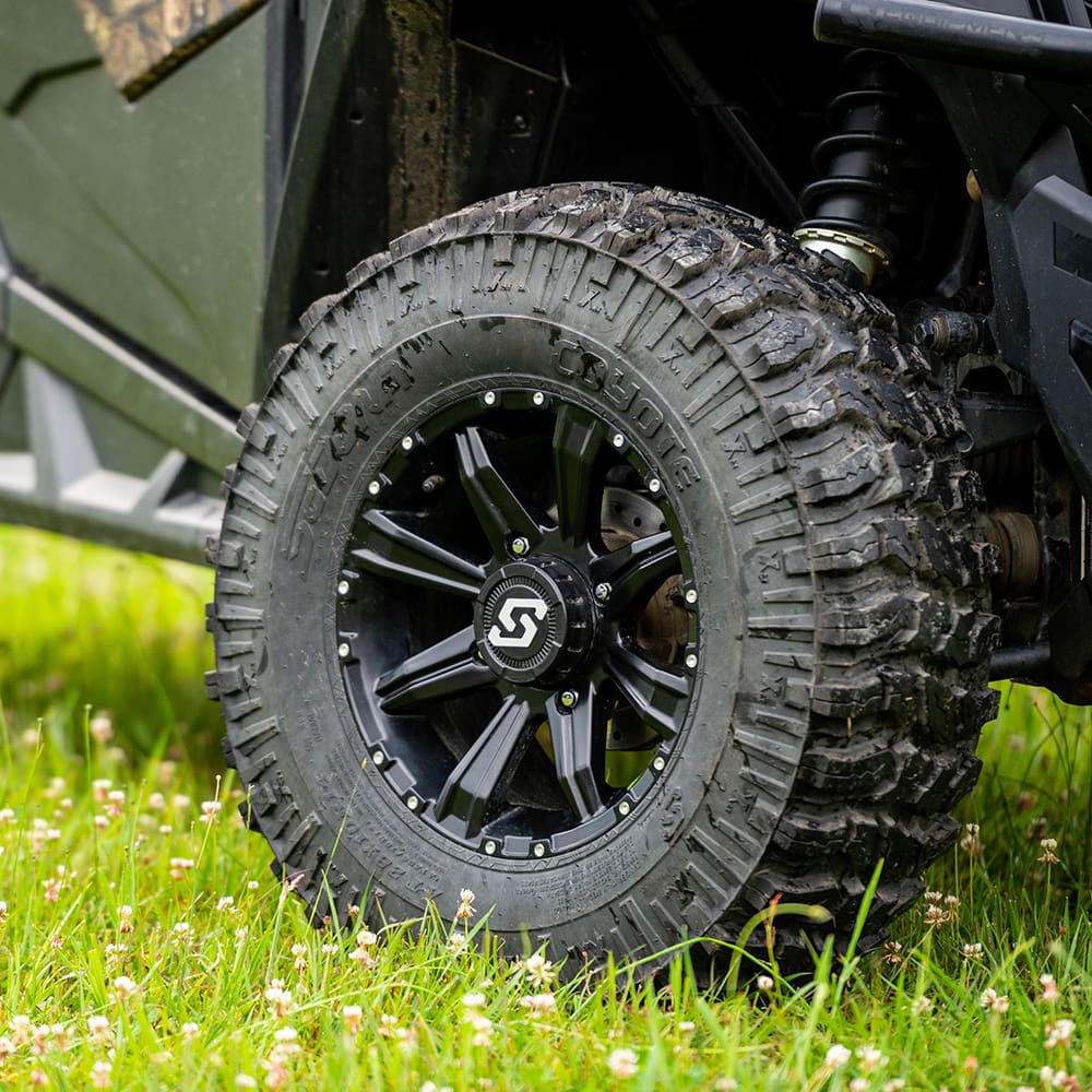 A Sedona Coyote 28x10R14 UTV 8-Ply Radial tire mounted on a black 14x7 Sedona UTV wheel, installed on a Polaris SXS parked in the grass.
