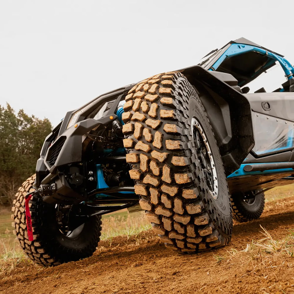 A close up view of the SuperATV Incursion AT tire mounted on a UTV, parked on a dirt trail, parked at an angle.