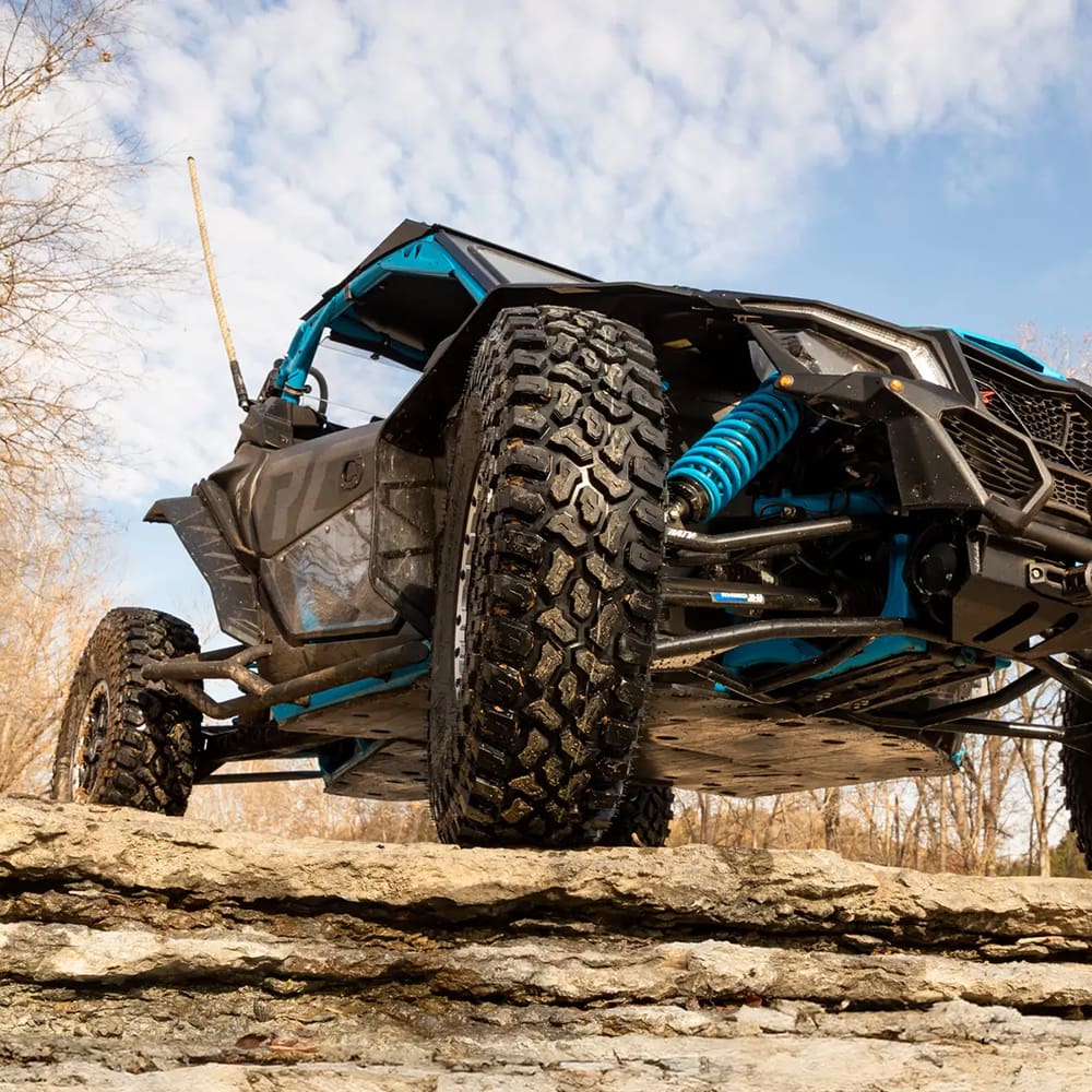 A close up view of the SuperATV Incursion AT tire mounted on a UTV, parked on a rocky ledge.
