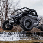 A full angled view of a Segway UTV with SuperATV XT Warrior sticky compound tires mounted on matte black beadlock rims, parked on a rocky wet ledge in a creek.