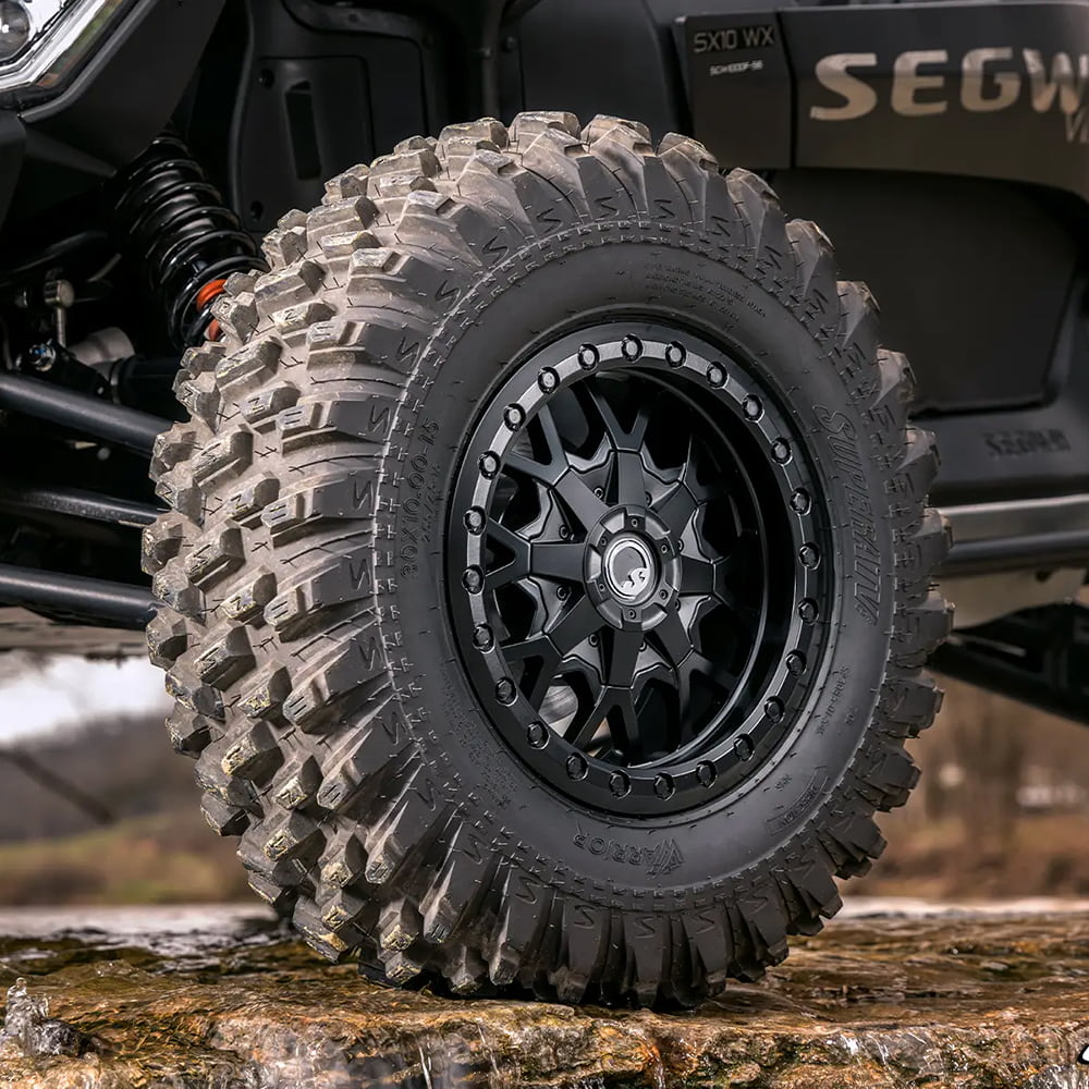 A close up view of a SuperATV XT Warrior tire mounted on a SuperATV beadlock wheel on a Segway SX10 SXS, parked on a rocky wet ledge.