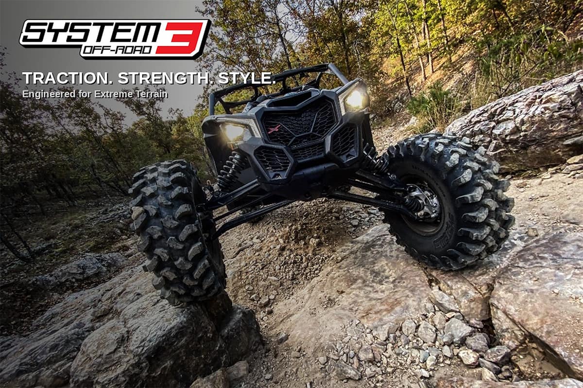 System 3 brand snippet image showing a Polaris RZR rock crawling on System 3 XTR370 tires, with a logo and tagline superimposed on the image in the top left corner reading "Traction. Strength. Style. Engineered for Extreme Terrain."