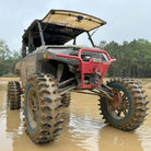 Set of 4 System3 XT400W extra wide mud and bog deep lug tires mounted on a Polaris RZR parked in a giant mud puddle.