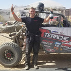 Side-by-side racer celebrating beside his Polaris RZR in the desert, featuring the Terache Stryker race tires.